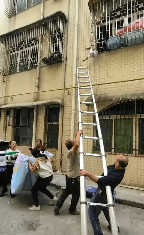 幼童脖子卡防盗窗悬空挂在墙外，有人撑被子有人架梯子，热心工人将她托举回屋内