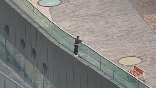 小伙站在城市阳台围栏外，身下踩的是仅有一个脚掌的外沿！